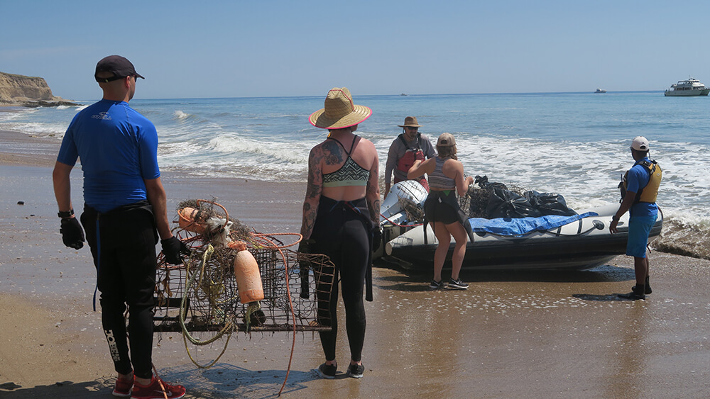 people hull marine debris off of a raft on a beach