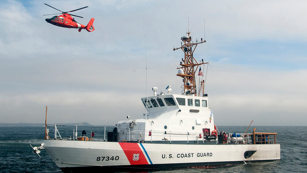 A coast guard ship, with a coast guard helicopter flying above