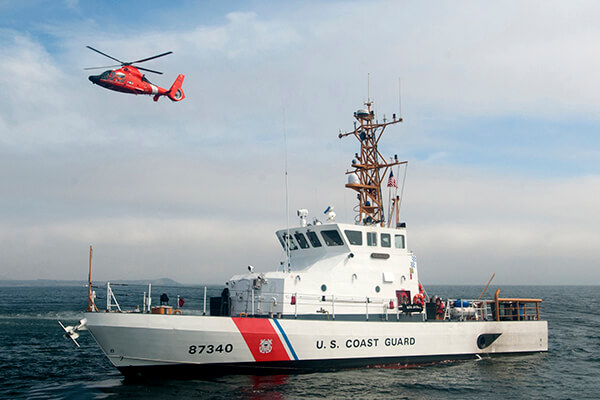 A coast guard helicopter flies past a coast guard ship