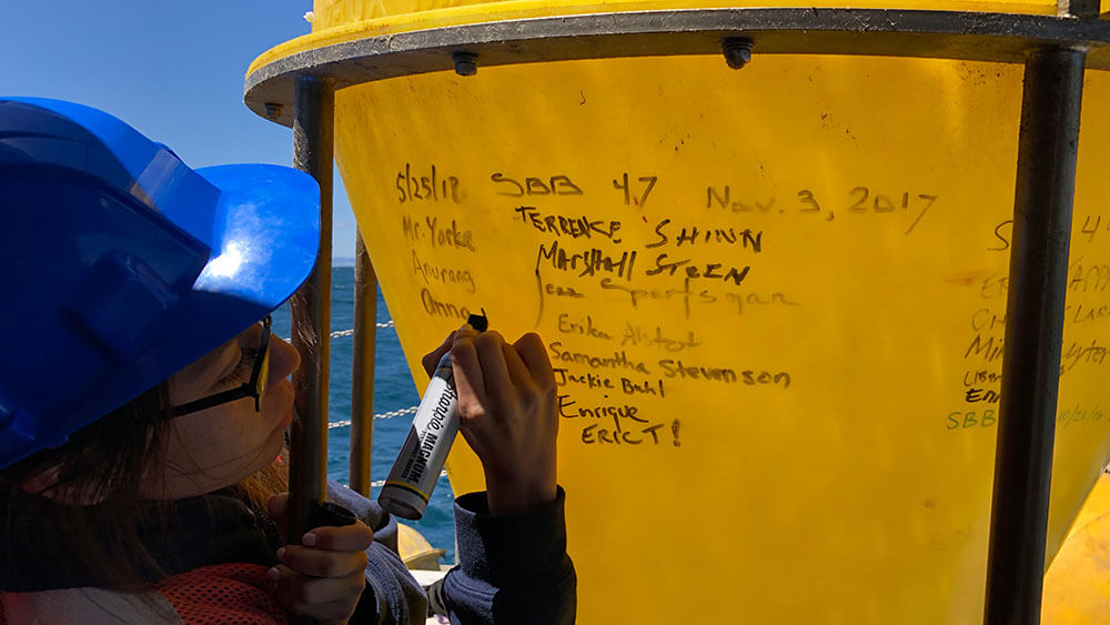 a student in a hard hat writing with permanent marker on a sediment trap