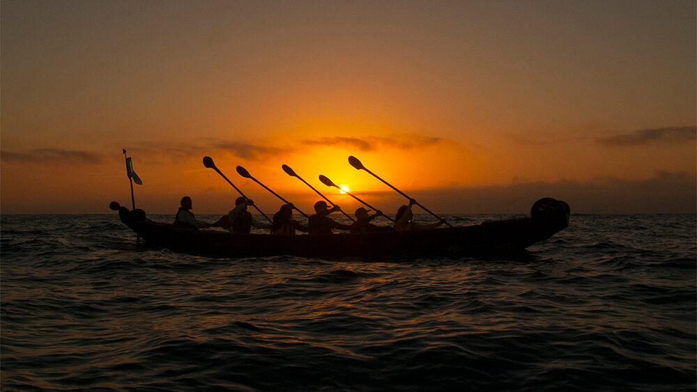 people row a tomol at sunrise